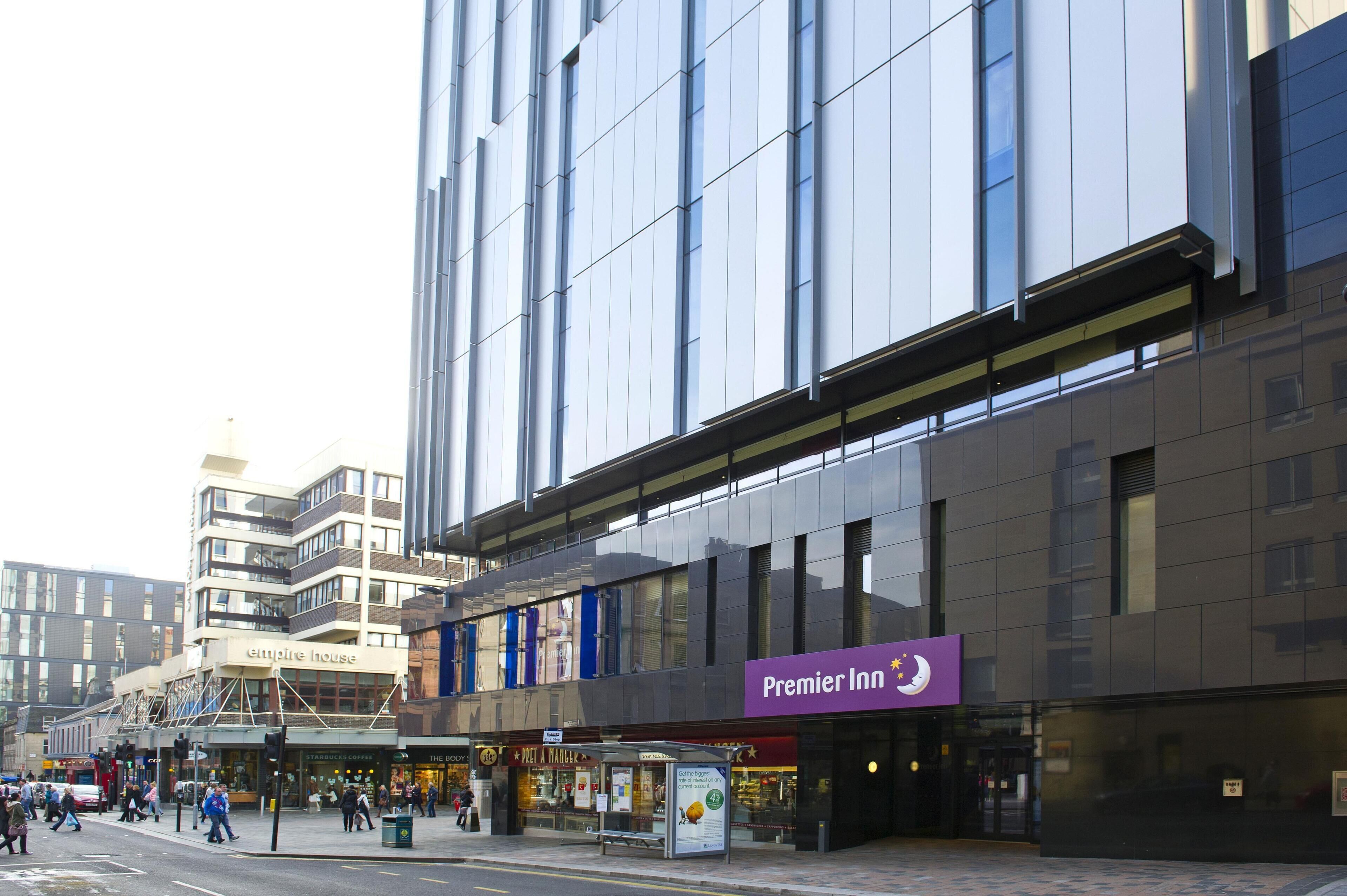 Un edificio moderno con un llamativo rótulo de Premier Inn, una entrada visible y un área peatonal a nivel de calle.