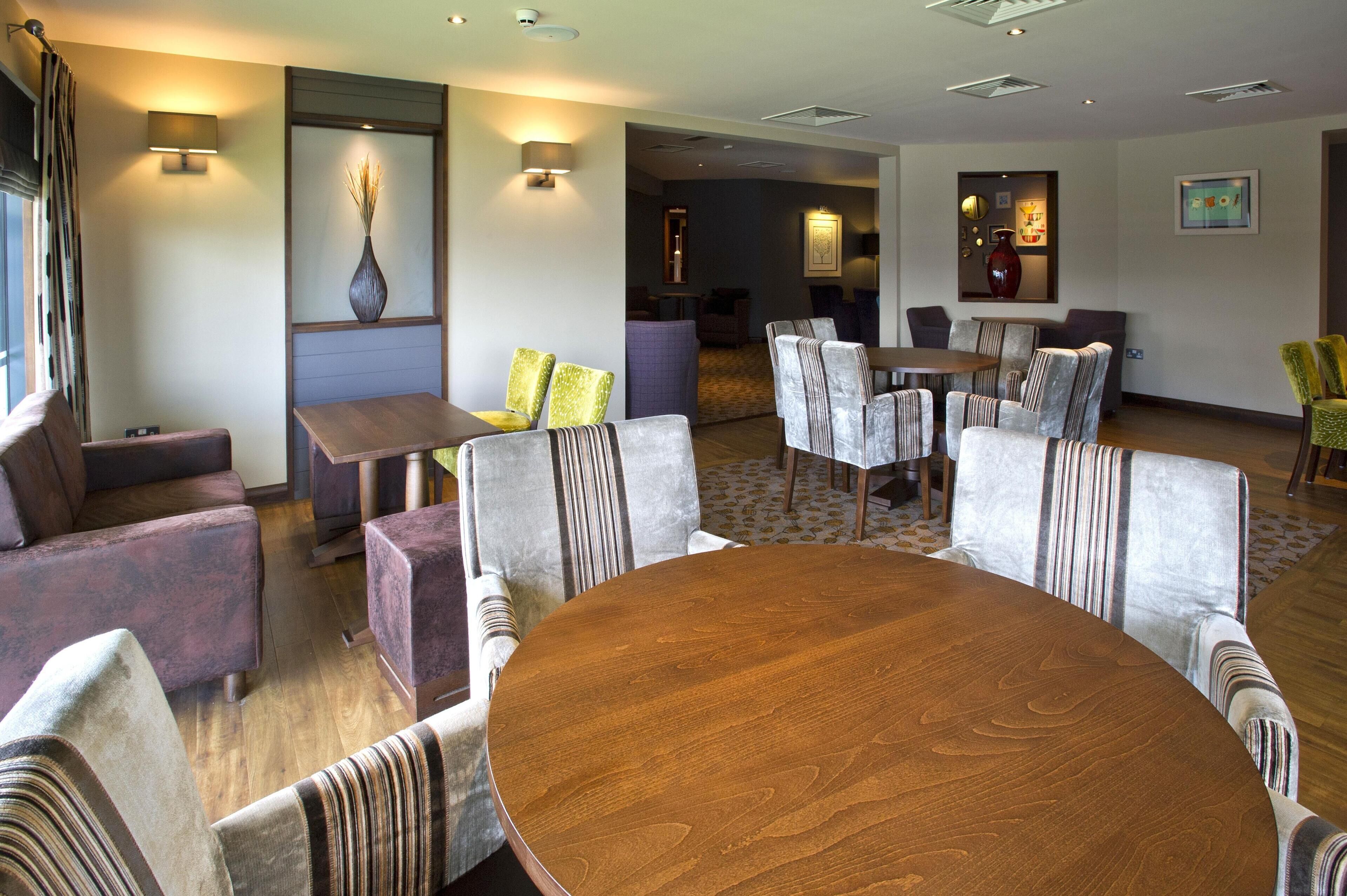 Un vestíbulo de hotel con una mesa redonda de madera, sillas a rayas, un sofá y un jarrón en la pared.