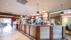 Una zona de bar con una barra alargada, varias luces colgantes y una variedad de bebidas y aperitivos.