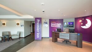 Zona de recepción de hotel con mostrador de registro, un área de descanso con sillas, un gran letrero de 'Premier Inn' y un letrero de 'Good Night Guarantee'.