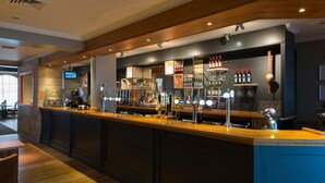 A bar area with a long counter, multiple taps, and shelves stocked with bottles. - Premier Inn Hull North (Hull)