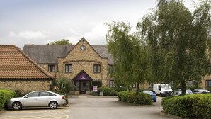 A building with a clock tower, a parking lot, and a car parked in front. - Premier Inn Hull West (Hessle)