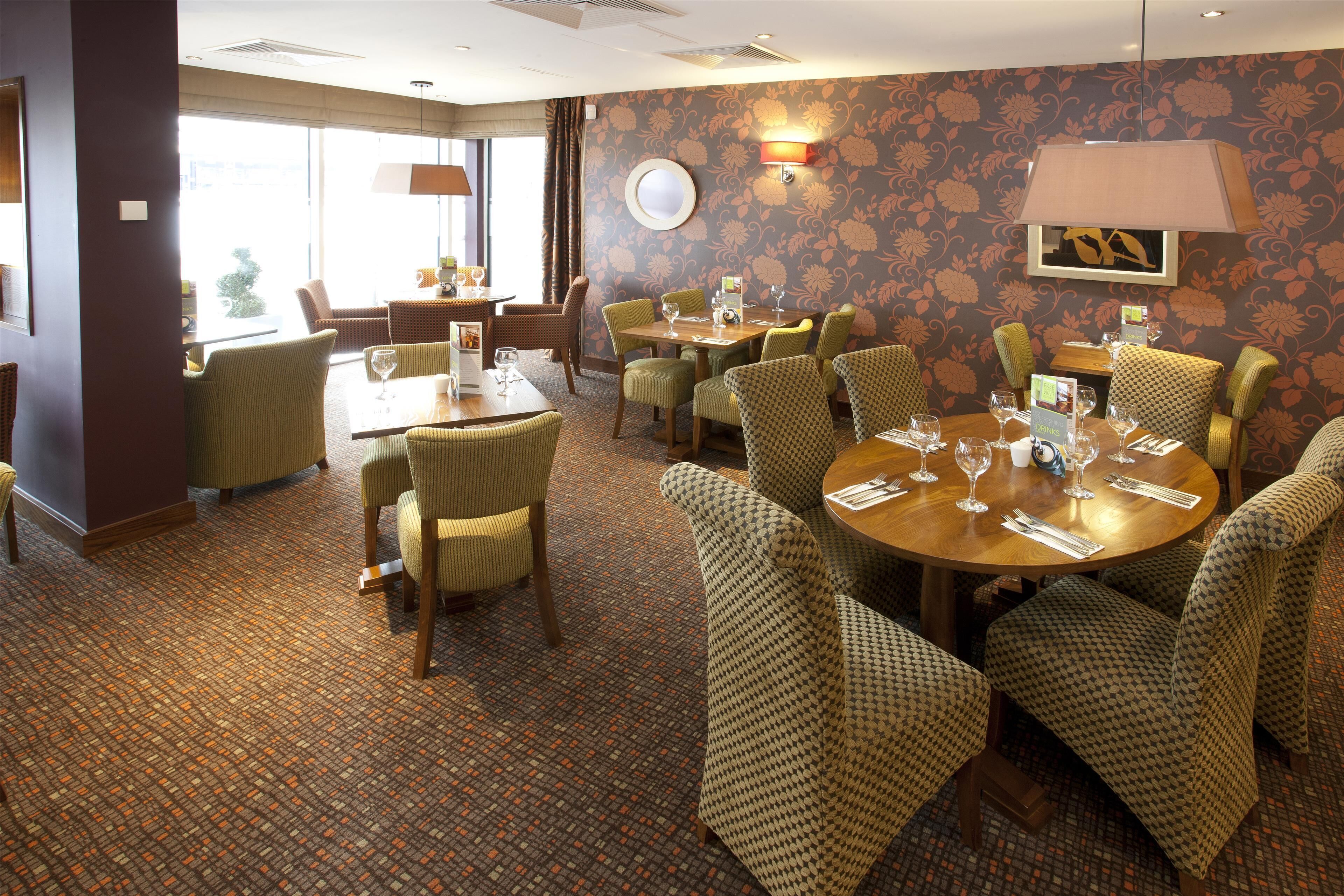 A hotel dining area with round tables, chairs, and a patterned carpet.