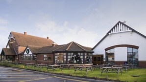 A building with a large arched entrance, a smaller attached structure with a gabled roof, and several picnic tables in front.