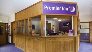 Ein hölzerner Premier Inn Empfangstresen mit einem violetten Schild, einem Computer und einer 'Wire-less'-Broschüre.