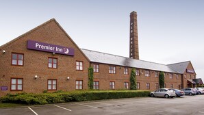 A Premier Inn hotel with a brick facade, multiple windows, and a parking lot with cars. - Premier Inn Leeds South - Birstall (Bradford)