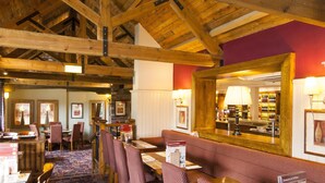 A restaurant with wooden beams, red upholstered seating, and a bar area. - Premier Inn Leeds South - Birstall (Bradford)