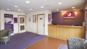 A hotel reception area with a wooden counter, two patterned chairs, and a purple carpet. - Premier Inn Leeds East (Leeds)