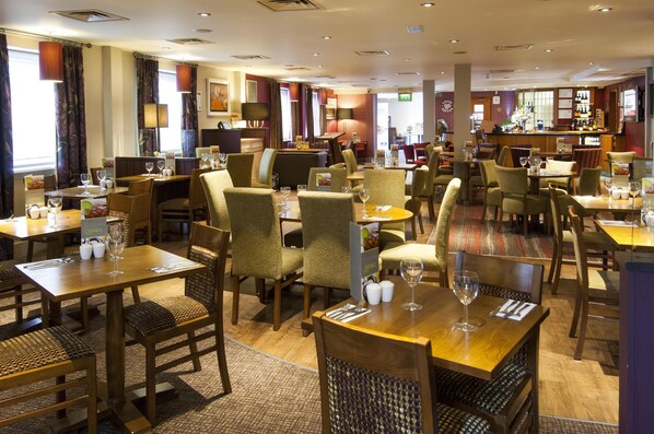A hotel restaurant with multiple dining tables and chairs, a bar area, and a view of the city. - Premier Inn Leeds City - Elland Road (Leeds)
