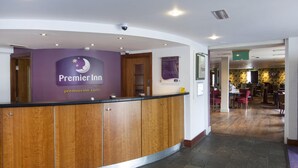 Ein Hotelrezeptionstresen mit einer Holzauskleidung, einem Schild für Premier Inn und Blick in den Speisesaal.