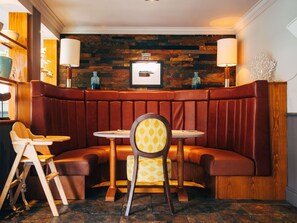 A restaurant with a booth seating area, wooden tables, and a brick wall backdrop.