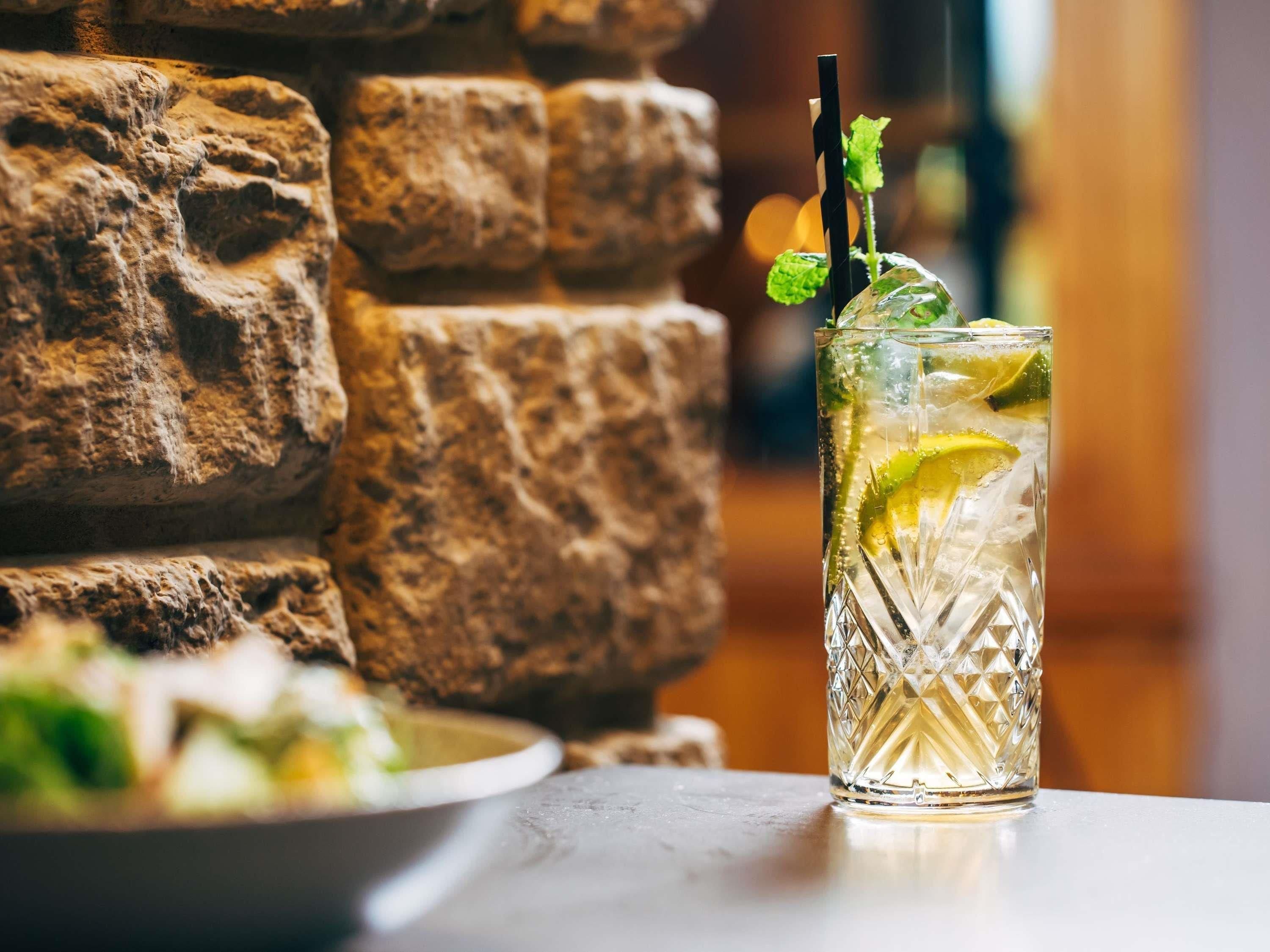 A glass of iced drink with lime and mint garnish on a table with a stone wall backdrop.