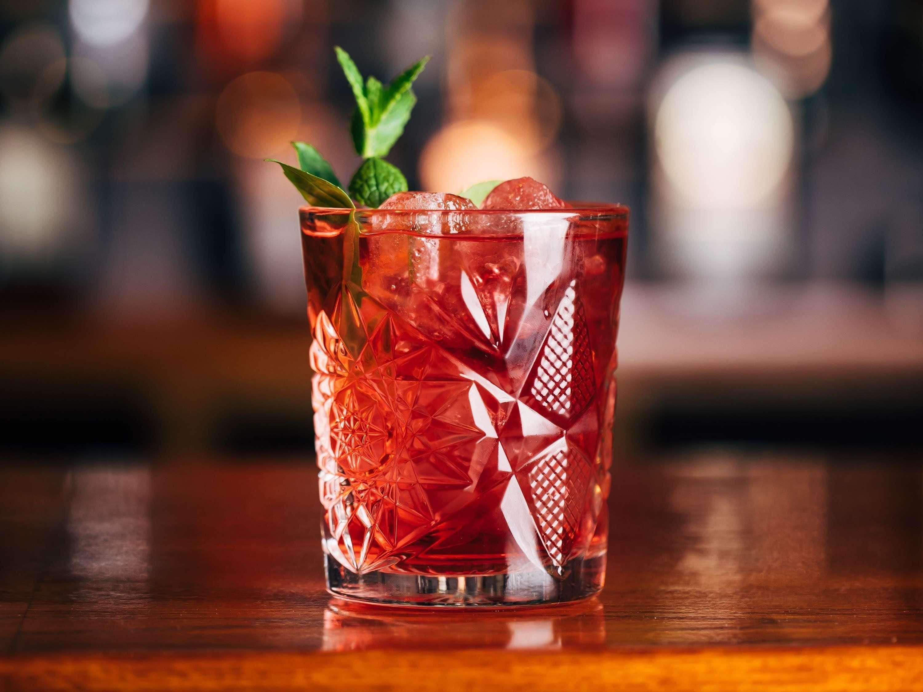 A clear glass with a geometric pattern, filled with a red beverage, ice cubes, and a mint leaf garnish.