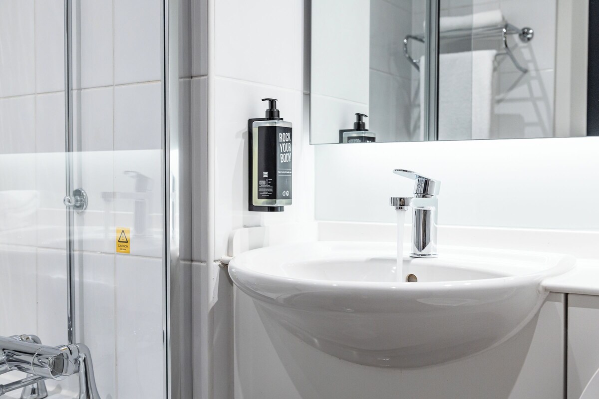 A modern bathroom with a white sink, chrome faucet, and a glass shower enclosure.