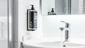 A bathroom with a white sink, chrome faucet, and a bottle of body lotion on the wall. - ibis Coleraine Riverside (Coleraine)
