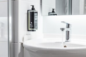 A bathroom with a white sink, chrome faucet, and a bottle of body lotion on the wall. - ibis Coleraine Riverside (Coleraine)