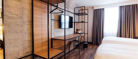 A modern hotel room with a wooden desk, a television, a bed, and a window with curtains.