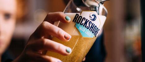 Eine Hand hält ein Bierglas mit dem Aufkleber 'Rockshore Irish Lager'.