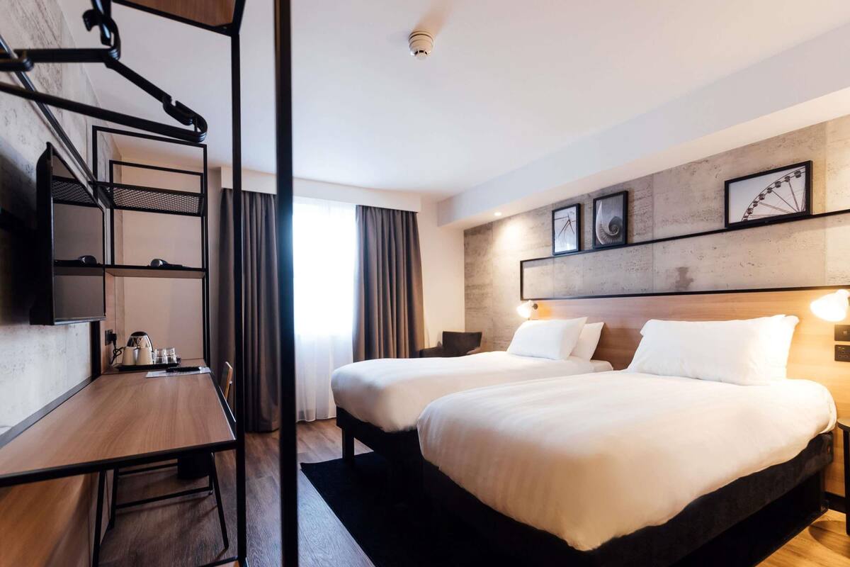 Ein Hotelzimmer mit zwei Betten, einem Schreibtisch mit Stuhl, einem Fernseher und einem Kleiderschrank.
