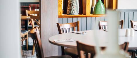 A restaurant interior with wooden chairs, a round table, and a green vase on the table.