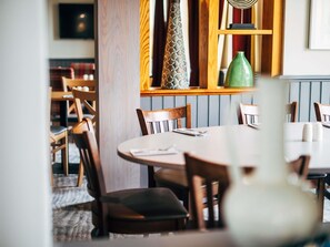A restaurant interior with wooden chairs, a round table, and a green vase on the table.