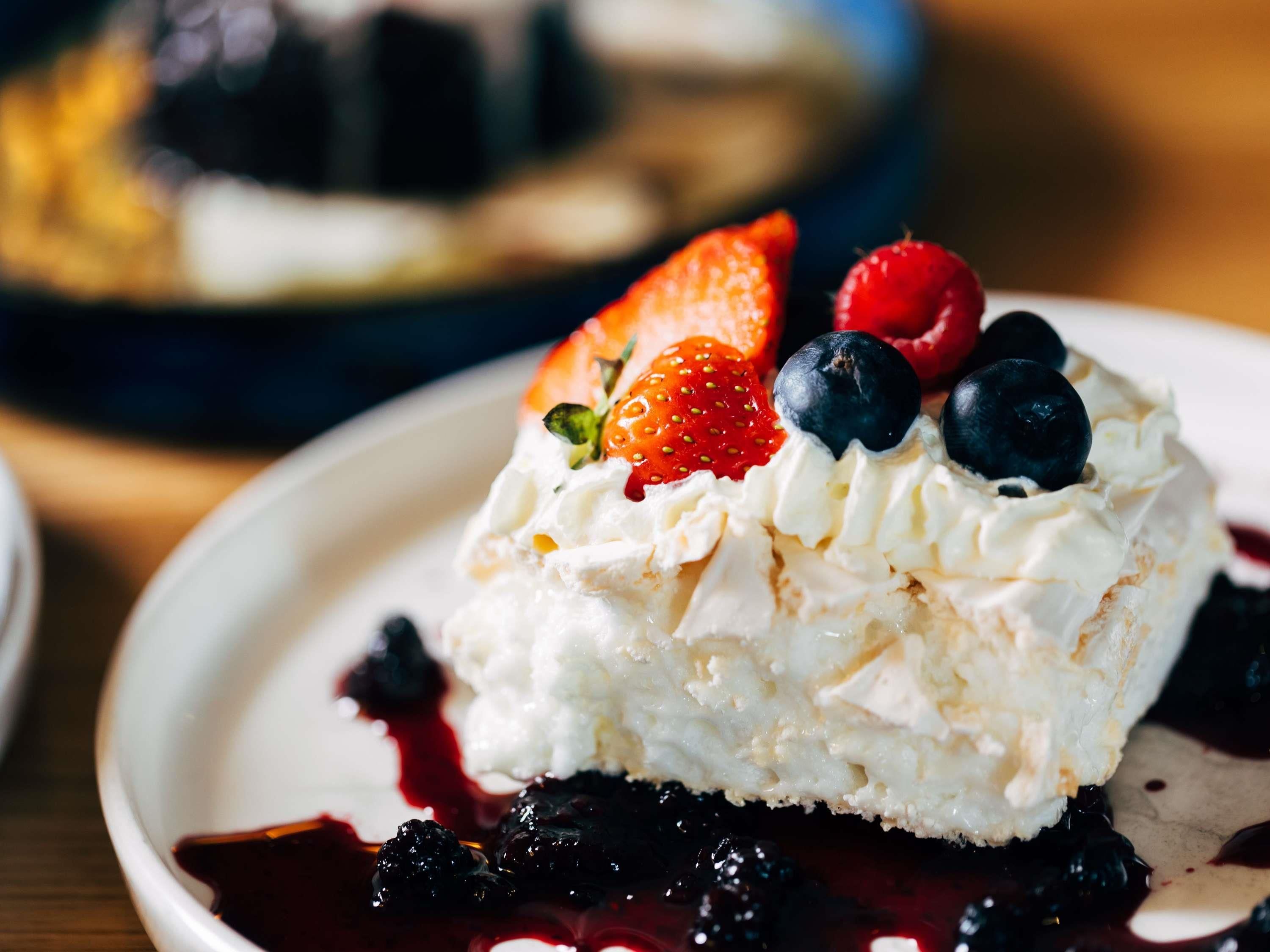 Un dessert composé de crème fouettée, de fraises et de myrtilles, présenté dans une assiette.