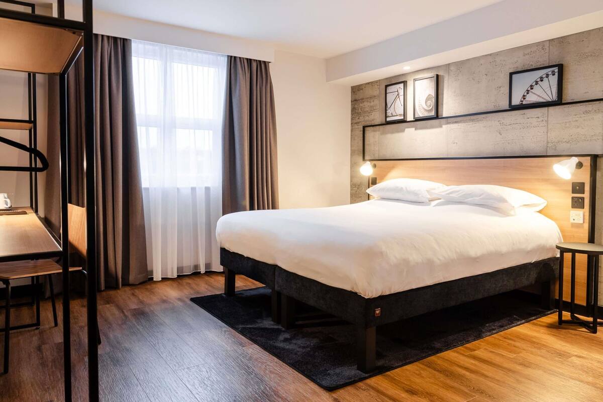 Ein modernes Hotelzimmer mit einem großen Bett, einem Schreibtisch und einem Fenster mit Vorhängen.