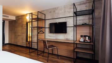 Habitación de hotel con cama, escritorio con silla, televisor montado en una pared texturizada y estantería con perchero.