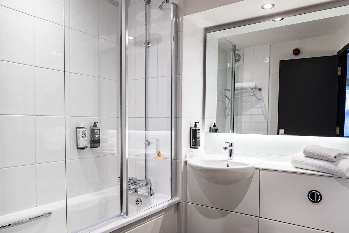 A modern bathroom with a glass shower enclosure, a white sink, and a large mirror.