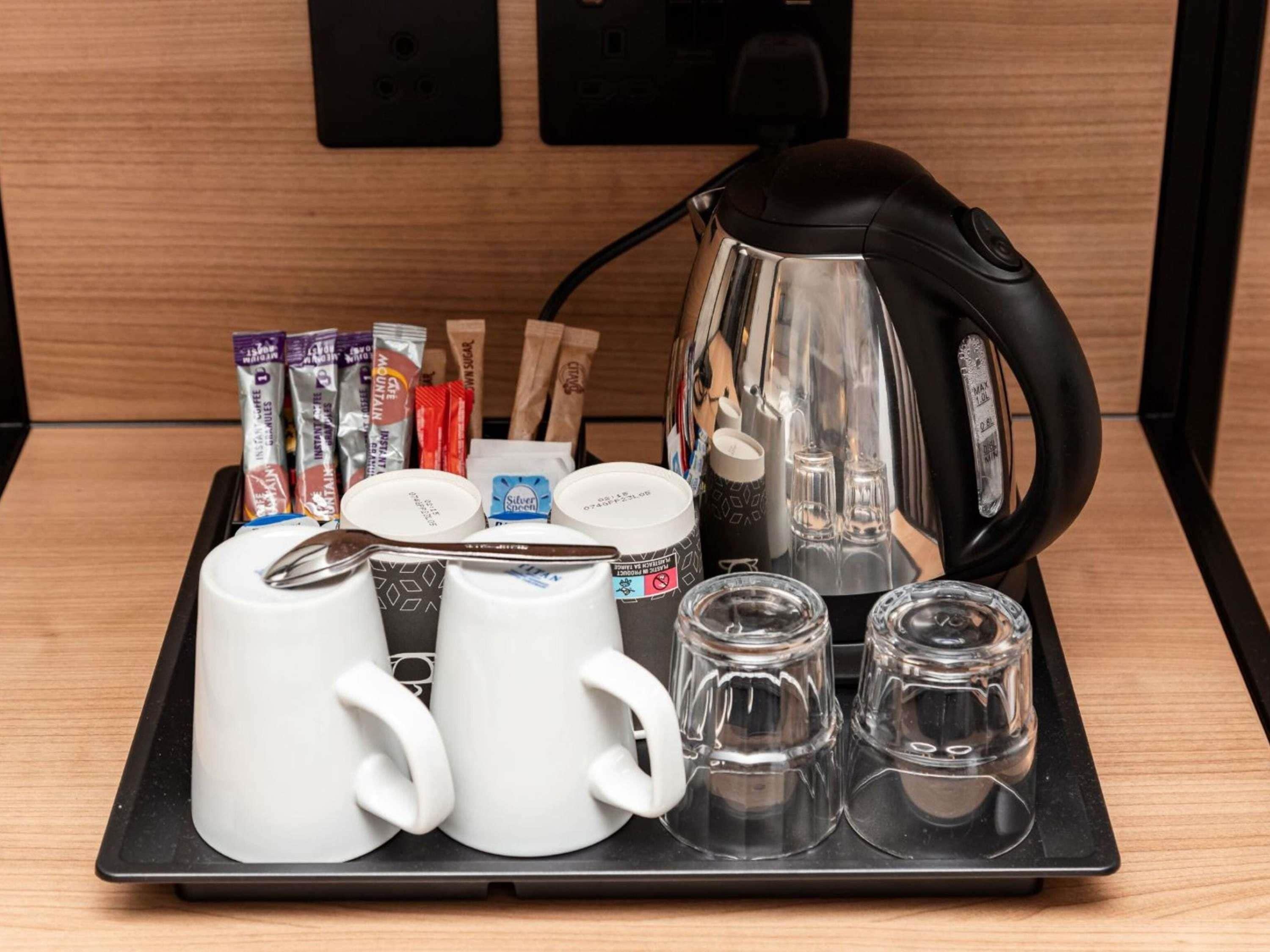 Un plateau avec des tasses à café, une bouilloire, des sachets de sucre et un pot à crème, posé sur une table en bois.