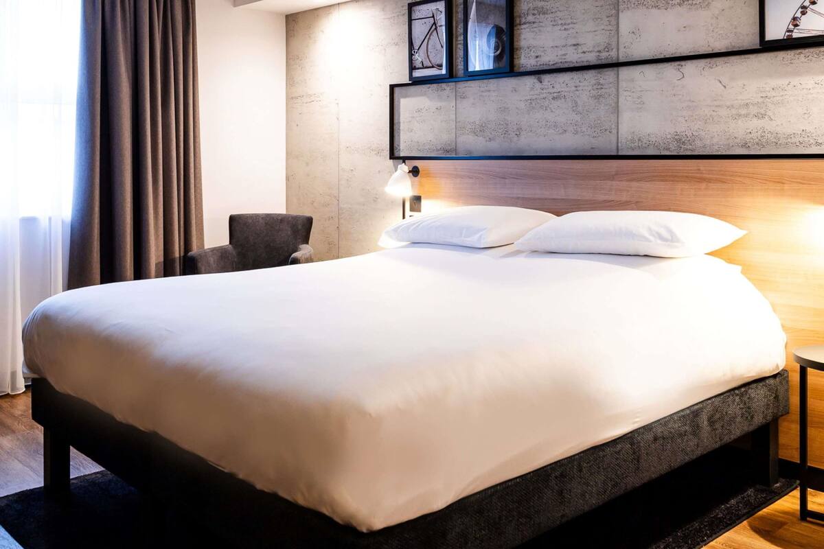 Ein modernes Hotelzimmer mit einem großen Bett, einem Sessel, einem Schreibtisch und einer Wandlampe.