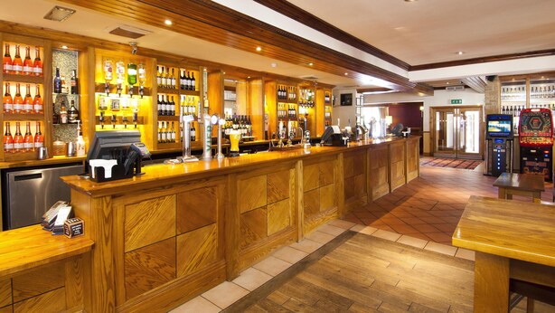 Een bar met houten lambrisering, een kassa en diverse flessen.