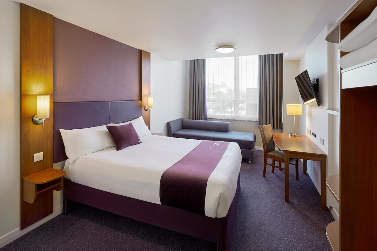Et hotelværelse med en stor seng, et skrivebord, en stol, en sofa og et fjernsyn på væggen.