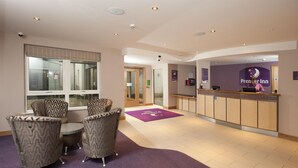 A hotel reception area with a reception desk, seating area with patterned chairs, and a reception wall with a logo. - Premier Inn Derry / Londonderry (Londonderry)