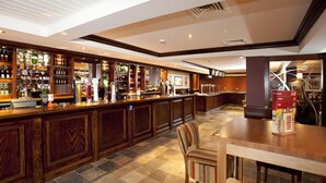 A bar area with a wooden counter, bar stools, and a variety of bottles. - Premier Inn Derry / Londonderry (Londonderry)