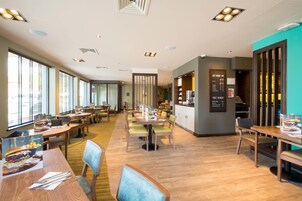 Un restaurante espacioso con mesas y sillas de madera, ventanas grandes y un panel con la carta.
