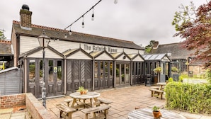 Gatwick Manor mit einer Terrasse, ausgestattet mit Holztischen und -bänken, einer Backsteinmauer und einem Schild über dem Eingang.