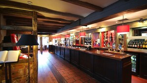 A bar area with wooden beams, a brick floor, and a long counter with various bottles and glasses. - Premier Inn East Grinstead (East Grinstead)
