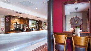 Een moderne hotelentree met een receptiebalie, een zithoek en een grote spiegel die het interieur weerspiegelt.