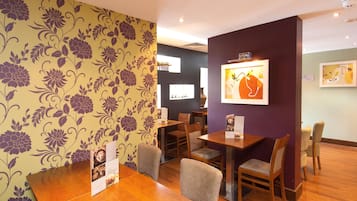 Un interior de restaurante con mesas y sillas de madera, papel tapiz floral y obras de arte enmarcadas en las paredes.