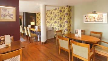 A hotel dining area with wooden tables and chairs, a reception desk, and a wall with a floral pattern.