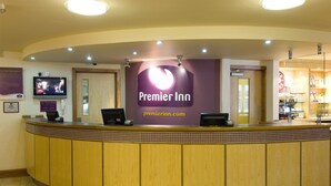 Un comptoir d’accueil d’hôtel avec une enseigne « Premier Inn » bien visible, un téléviseur fixé au mur et un comptoir équipé d’un ordinateur et d’un téléphone.