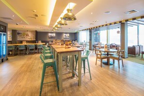 A restaurant with wooden flooring, green bar stools, and a variety of seating options including tables and chairs. - Premier Inn Lichfield City Centre (Lichfield)
