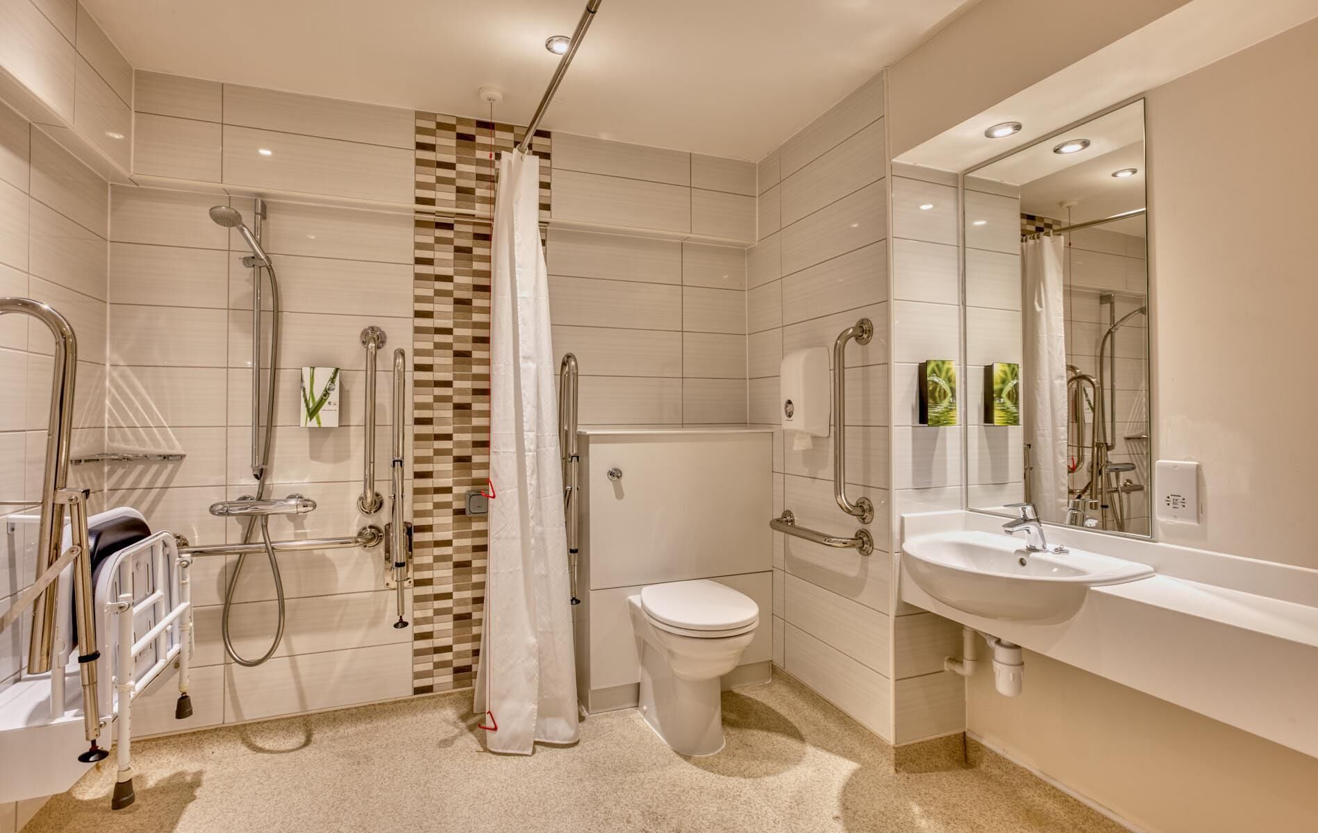 A modern bathroom with a shower, toilet, and sink, equipped with grab bars and a hand dryer.