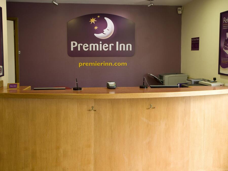 A reception desk at Premier Inn with a sign above it, a computer, and a telephone.