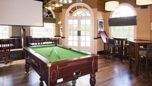 Ein Billardtisch mit grüner Spielvliesdecke, Holzrahmen und Deckenleuchten.