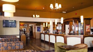 Eine Hotellobby mit Barbereich, Sitzgelegenheiten mit gemusterten Polstern und einem an der Wand befestigten Fernseher.