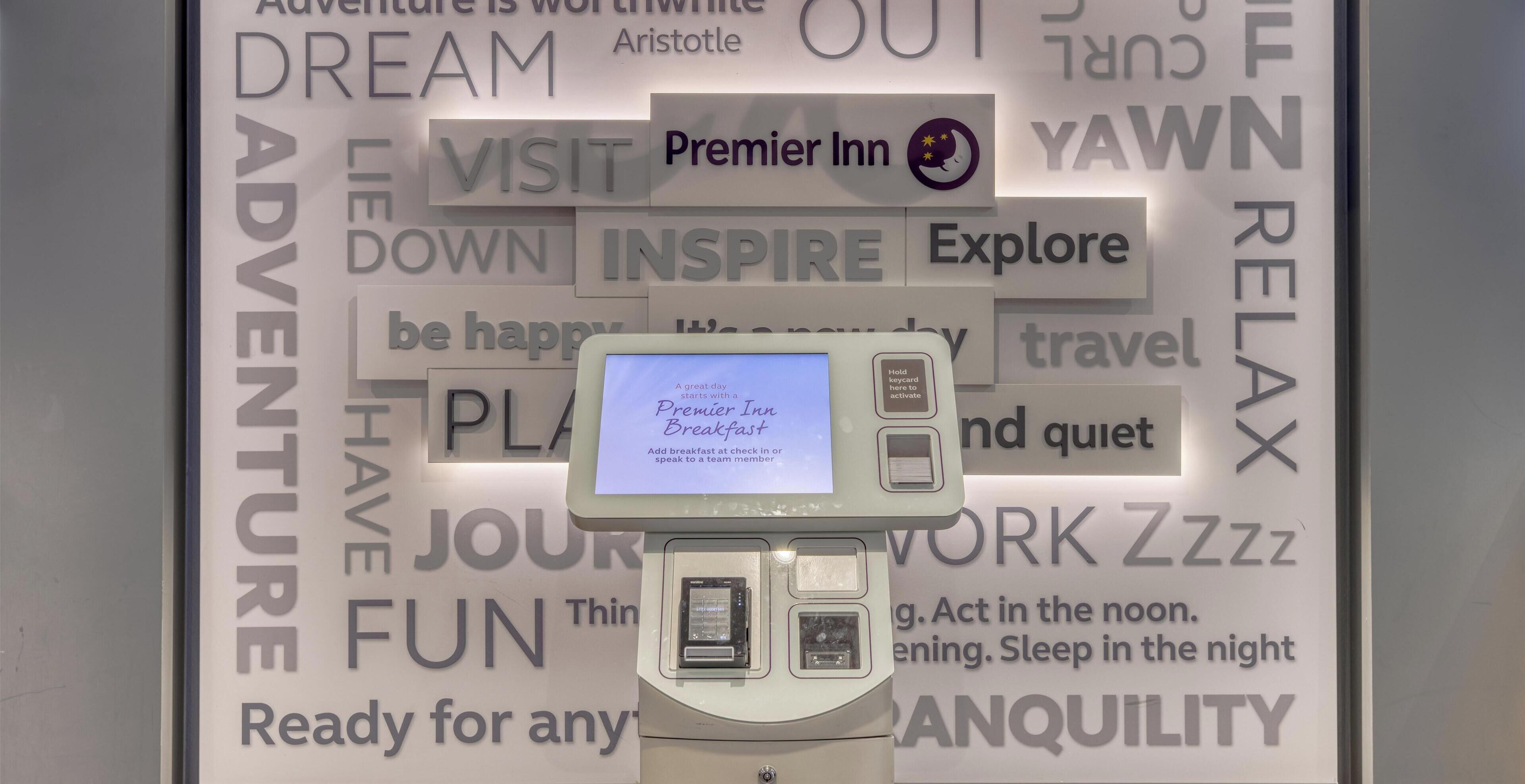 A Premier Inn sign with a digital screen displaying 'A great day. Add breakfast at check-in speak to a team member.'