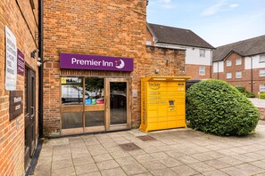 A brick building with a purple sign for Premier Inn, a yellow Amazon Locker, and a green hedge. - Premier Inn London Harrow (Harrow)