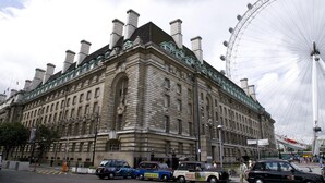 Un edificio histórico con una imponente torre de reloj, una noria grande y una calle con coches estacionados.